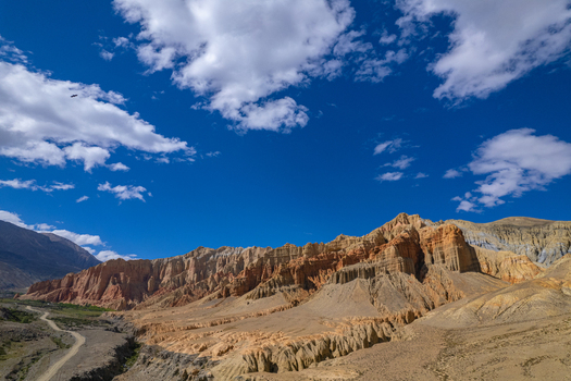 Aerial view of the rugged arid mountain landscape of the Mustang region with dramatic rock formations deep canyons and a winding dirt road under a bright blue sky in Nepal.