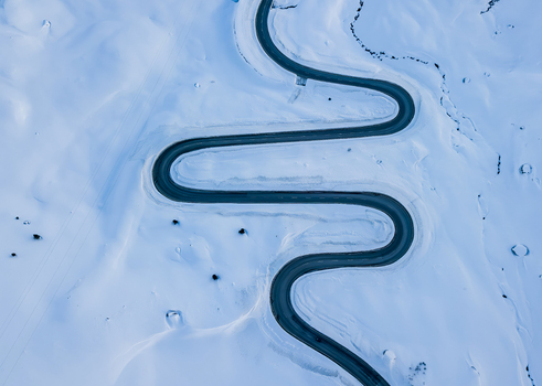 Aerial view of the winding road of Julier Pass cutting through a vast snow covered landscape in Surses Grisons Switzerland.