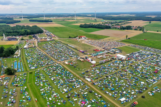 Aerial view of the Open Beatz Festival campsite with colorful tents parked cars and wind turbines across the rural landscape in Herzogenaurach Bayern Germany. Aerial view of the Open Beatz Festival campsite with colorful tents parked cars and wind turbines across the rural landscape in Herzogenaurach Bayern Germany.