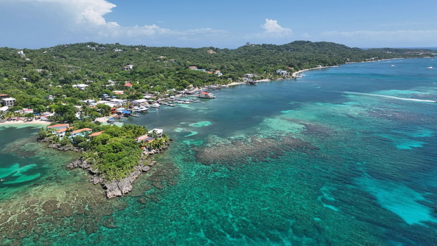 Aerial view of the coastal village of West End with turquoise waters coral reefs lush green hills and small boats docked along the shore in West End Bay Islands Department Honduras.