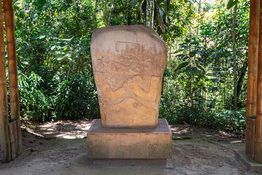 View of an ancient stone statue at San Agustin Archaeological Park surrounded by lush green forest and bamboo supports San Agustin Huila Colombia.