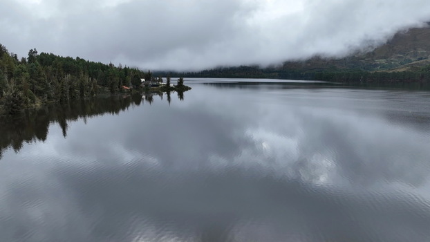 Aerial view of Corani Lake with calm water reflecting the overcast sky surrounded by dense pine forests and misty mountains in Chapare Cochabamba Department Bolivia. Aerial view of Corani Lake with calm water reflecting the overcast sky surrounded by dense pine forests and misty mountains in Chapare Cochabamba Department Bolivia.