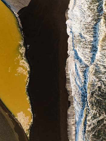Aerial view of the dramatic contrast between a yellow river and a black sand beach where waves crash against the shore in Reykjanesbaer Iceland. Aerial view of the dramatic contrast between a yellow river and a black sand beach where waves crash against the shore in Reykjanesbaer Iceland.