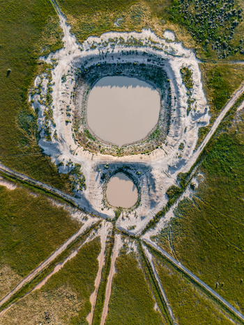 Aerial view of two circular ponds surrounded by sandy banks and green fields with dirt tracks in the flat landscape of Hay New South Wales Australia.