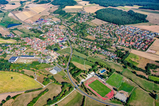 Aerial view of the town of Burghaslach featuring red roofed houses lush green fields dense forests and a sports stadium in Burghaslach Bavaria Germany.