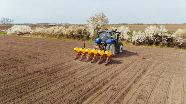 Aerial view of a blue tractor amidst the brown earth and white blossomed trees planting seeds in the field Sremska Mitrovica Vojvodina Serbia. Aerial view of a blue tractor amidst the brown earth and white blossomed trees planting seeds in the field Sremska Mitrovica Vojvodina Serbia.