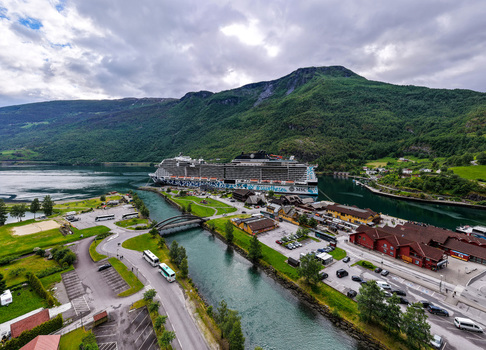 Flam Norway 18 June 2026 Aerial view of a large cruise ship docked in the Aurlandsfjord at Flam surrounded by steep green mountains a river and small buildings under a cloudy sky. Flam Norway 18 June 2026 Aerial view of a large cruise ship docked in the Aurlandsfjord at Flam surrounded by steep green mountains a river and small buildings under a cloudy sky.