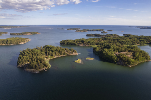 Aerial view of the Espoo archipelago with lush green islands rocky shorelines and calm blue waters under a clear sky in Espoo Uusimaa Finland.