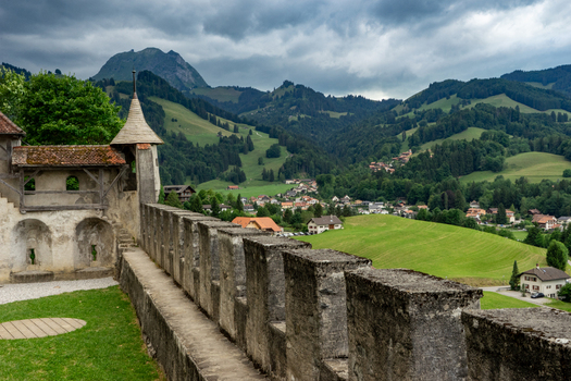 Gruyeres Switzerland 14 May 2026 View of Gruyeres Castle stone walls and crenellations overlooking the green valley village houses and the Swiss Prealps under a cloudy sky. Gruyeres Switzerland 14 May 2026 View of Gruyeres Castle stone walls and crenellations overlooking the green valley village houses and the Swiss Prealps under a cloudy sky.