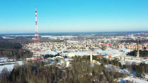 Aerial view of a tall radio tower standing above a snow covered town with surrounding forests and a clear blue sky in Latvia. Aerial view of a tall radio tower standing above a snow covered town with surrounding forests and a clear blue sky in Latvia.