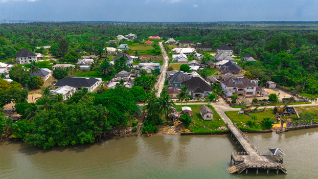 Aerial view of a riverside village with scattered houses lush vegetation and a wooden pier extending into the water Minima Rivers Nigeria.
