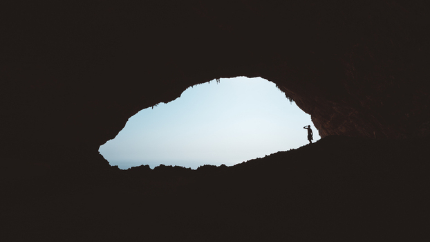 View of a person silhouetted against the bright entrance of Hoq Cave with rugged rock formations and natural light in Socotra Socotra Yemen. View of a person silhouetted against the bright entrance of Hoq Cave with rugged rock formations and natural light in Socotra Socotra Yemen.