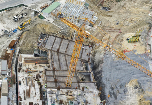 Aerial view of a construction site with a large yellow tower crane workers on a rebar foundation and heavy machinery in Sariyer Istanbul Turkiye. Aerial view of a construction site with a large yellow tower crane workers on a rebar foundation and heavy machinery in Sariyer Istanbul Turkiye.