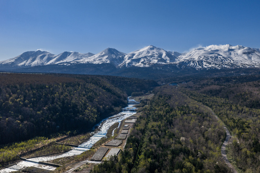 Aerial view of the river flowing through the forested valley with snow capped mountains in the background in Furano Hokkaido Japan. Aerial view of the river flowing through the forested valley with snow capped mountains in the background in Furano Hokkaido Japan.
