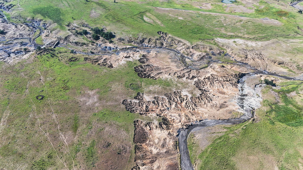 Aerial view of severe soil erosion and deep gullies cutting through green grassy hills and a winding stream bed in Pietermaritzburg KwaZulu Natal South Africa.