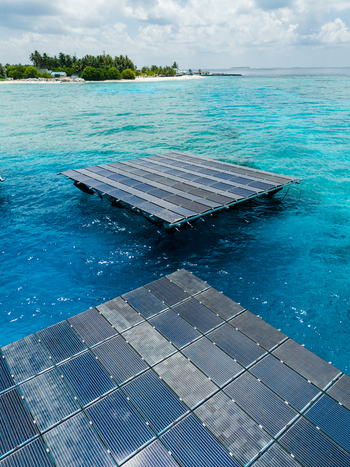 Aerial view of SolarSea floating solar power plant on turquoise water with a tropical island in the background Dharavandhoo Baa Atoll Maldives. Aerial view of SolarSea floating solar power plant on turquoise water with a tropical island in the background Dharavandhoo Baa Atoll Maldives.