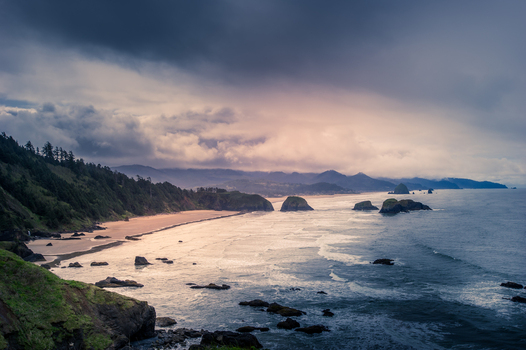 View of the rugged coastline at Cannon Beach with Haystack Rock sandy beach dark storm clouds and Pacific Ocean waves in Cannon Beach Oregon United States. View of the rugged coastline at Cannon Beach with Haystack Rock sandy beach dark storm clouds and Pacific Ocean waves in Cannon Beach Oregon United States.