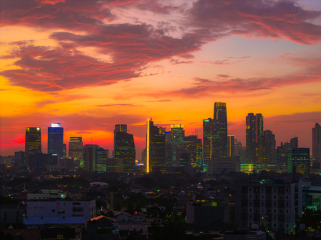 Aerial view of the Jakarta skyline at sunset with illuminated skyscrapers and vibrant orange and purple clouds over the city Tebet Jakarta Indonesia.
