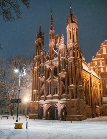 View of the illuminated Gothic facade of St. Anne s Church during a winter night with snow covered ground in Vilnius Vilnius County Lithuania. View of the illuminated Gothic facade of St. Anne s Church during a winter night with snow covered ground in Vilnius Vilnius County Lithuania.