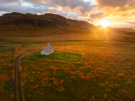 Aerial view of a solitary white church standing proudly amidst golden fields under a dramatic sunset framed by dark mountains Snæfellsnes Eyja og Miklaholtshreppur Iceland. Aerial view of a solitary white church standing proudly amidst golden fields under a dramatic sunset framed by dark mountains Snæfellsnes Eyja og Miklaholtshreppur Iceland.