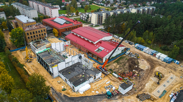 Aerial view of a construction site featuring a crane building framework and adjacent buildings with red roofs in Latvia. Aerial view of a construction site featuring a crane building framework and adjacent buildings with red roofs in Latvia.