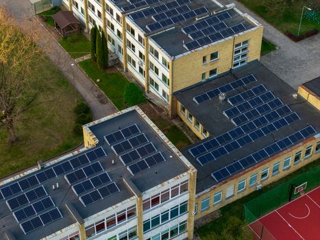 Aerial view of solar panels installed on the flat rooftops of a modern building next to a red basketball court and green lawn Vilnius County Lithuania. Aerial view of solar panels installed on the flat rooftops of a modern building next to a red basketball court and green lawn Vilnius County Lithuania.