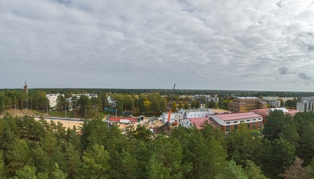 Aerial view of a construction site with a crane surrounded by dense pine forests and nearby residential buildings in Latvia. Aerial view of a construction site with a crane surrounded by dense pine forests and nearby residential buildings in Latvia.