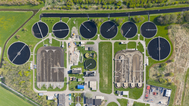 Aerial view of RWZI Geestmerambacht water treatment plant with circular tanks and rectangular basins surrounded by green fields and trees in the Netherlands. Aerial view of RWZI Geestmerambacht water treatment plant with circular tanks and rectangular basins surrounded by green fields and trees in the Netherlands.