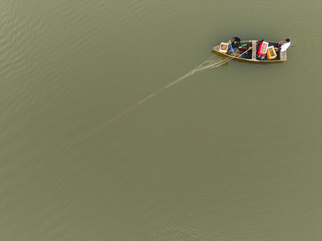 Aerial view of two fishermen in a small wooden boat pulling a fishing net on calm murky water in Galle Southern Province Sri Lanka. Aerial view of two fishermen in a small wooden boat pulling a fishing net on calm murky water in Galle Southern Province Sri Lanka.
