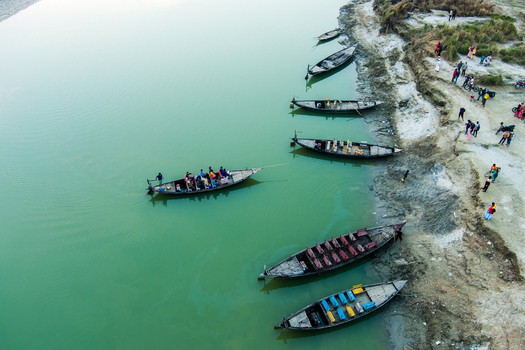 Aerial view of traditional wooden boats moored along the muddy riverbank with people walking nearby in Rajshahi Rajshahi Division Bangladesh.