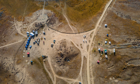 Aerial view of Deosai National Park featuring a remote campsite with colorful tents parked vehicles and winding dirt tracks across the vast high altitude plateau in Skardu Gilgit Pakistan.