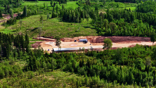 Aerial view of a wind turbine foundation and long white turbine blades resting on a dirt construction site surrounded by a dense green forest in Latvija. Aerial view of a wind turbine foundation and long white turbine blades resting on a dirt construction site surrounded by a dense green forest in Latvija.