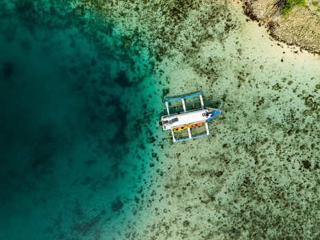 Aerial view of a traditional outrigger boat floating in the clear turquoise waters of Bucas Grande with coral reefs visible beneath the surface near the shore of Siargao Philippines. Aerial view of a traditional outrigger boat floating in the clear turquoise waters of Bucas Grande with coral reefs visible beneath the surface near the shore of Siargao Philippines.