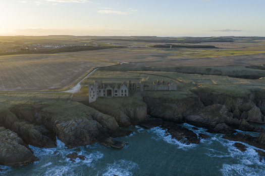 Aerial view of the ruins of Slains Castle on a rugged cliff edge overlooking the sea and crashing waves at sunset in Cruden Bay Scotland United Kingdom. Aerial view of the ruins of Slains Castle on a rugged cliff edge overlooking the sea and crashing waves at sunset in Cruden Bay Scotland United Kingdom.