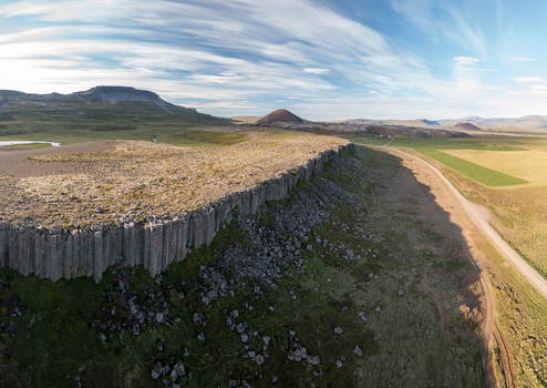 Aerial view of the basalt columns of Gerduberg Cliffs with a dirt road running alongside the grassy landscape under a bright blue sky Raudhamelur Eyja og Miklaholtshr Iceland. Aerial view of the basalt columns of Gerduberg Cliffs with a dirt road running alongside the grassy landscape under a bright blue sky Raudhamelur Eyja og Miklaholtshr Iceland.