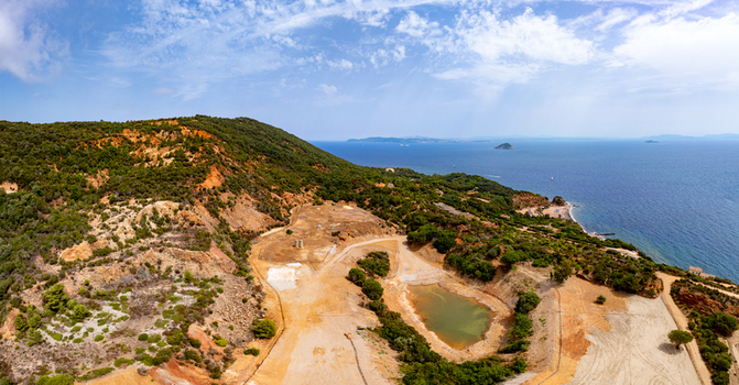 Aerial view of the historic iron mine area with reddish geology and the Laghetto delle conche pond surrounded by Mediterranean vegetation near the sea in Rio Marina Toscana Italy.