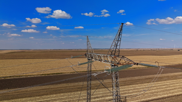 Aerial view of electric power transmission lines stretching across vast agricultural fields under a clear blue sky in Pancevo Serbia.