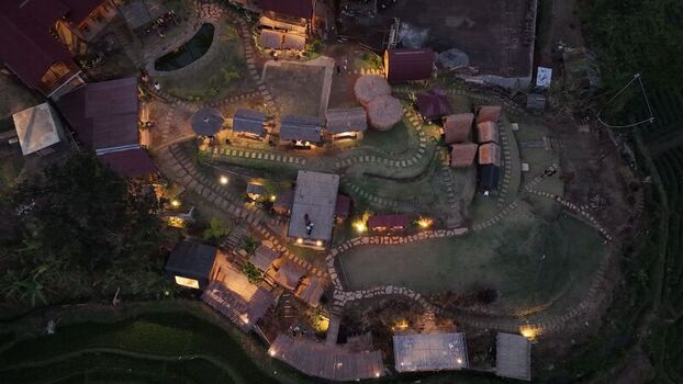 Aerial view of a resort area in Trawas with illuminated pathways small thatched roof structures and lush greenery at dusk in Trawas East Java Indonesia. Aerial view of a resort area in Trawas with illuminated pathways small thatched roof structures and lush greenery at dusk in Trawas East Java Indonesia.