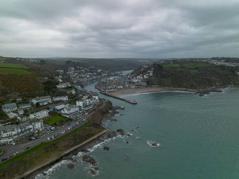 Aerial view of the coastal town of Looe featuring the harbour sandy beach rocky coastline and surrounding green hills under a cloudy sky in Looe Cornwall United Kingdom. Aerial view of the coastal town of Looe featuring the harbour sandy beach rocky coastline and surrounding green hills under a cloudy sky in Looe Cornwall United Kingdom.