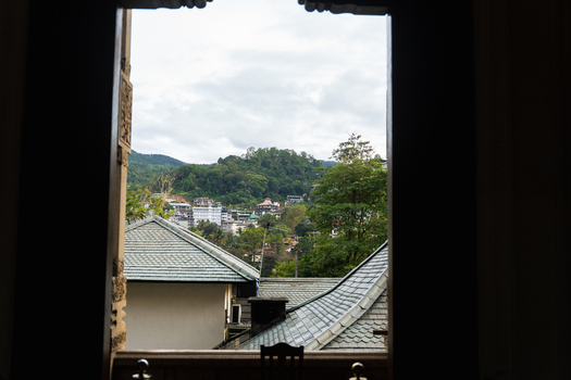 View of the urban landscape of Kandy through a dark window frame with lush green hills and rooftops under a cloudy sky Kandy Central Province Sri Lanka. View of the urban landscape of Kandy through a dark window frame with lush green hills and rooftops under a cloudy sky Kandy Central Province Sri Lanka.