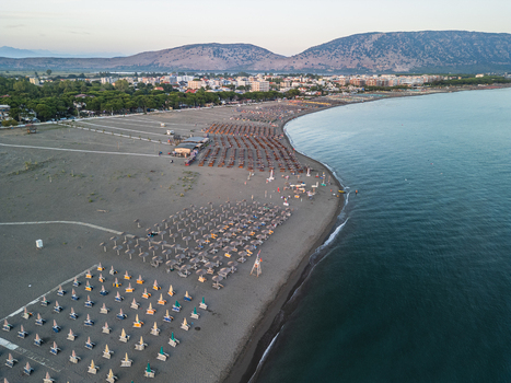 Aerial view of Velipoja Beach with rows of organized beach umbrellas on the sandy shore calm Adriatic Sea and distant mountains in Velipoje Shkoder County Albania.