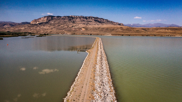 Aerial view of a long stone causeway dividing a calm reservoir with mountains in the background under a clear blue sky in Cody Wyoming United States. Aerial view of a long stone causeway dividing a calm reservoir with mountains in the background under a clear blue sky in Cody Wyoming United States.