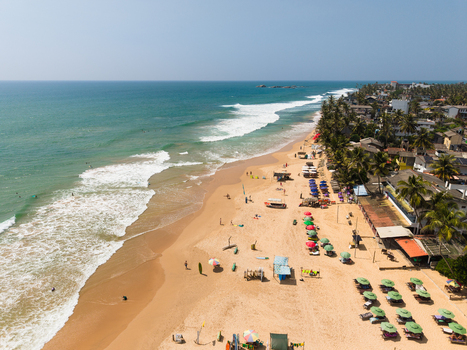Aerial view of the sandy coastline of Hikkaduwa Beach with turquoise ocean waves palm trees and colorful beach umbrellas Hikkaduwa Southern Province Sri Lanka. Aerial view of the sandy coastline of Hikkaduwa Beach with turquoise ocean waves palm trees and colorful beach umbrellas Hikkaduwa Southern Province Sri Lanka.