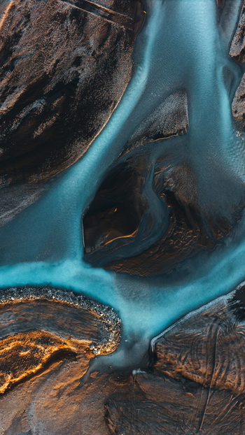 Aerial view of turquoise glacial braided rivers flowing through dark volcanic sediment and textured earth in Skaftarhreppur Iceland.