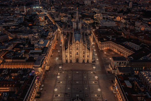 Milano Italy 06 July 2020 Aerial view of Duomo di Milano illuminated at night surrounded by the historic city center cobblestone square and glowing street lights. Milano Italy 06 July 2020 Aerial view of Duomo di Milano illuminated at night surrounded by the historic city center cobblestone square and glowing street lights.