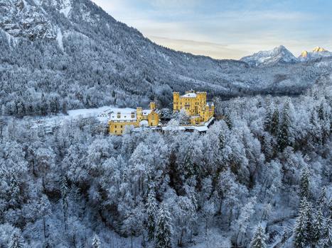 Aerial view of Hohenschwangau Castle perched atop a snow laden hill amidst the frosted forest Schwangau Bayern Germany.