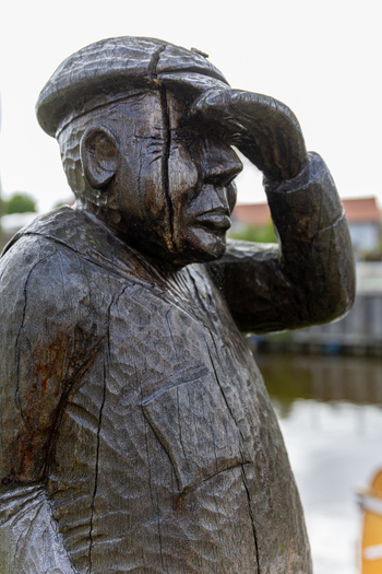 View of a wooden sculpture of a fisherman looking out over the water at Hafen Harlesiel with visible wood grain and a traditional cap Wittmund Lower Saxony Germany. View of a wooden sculpture of a fisherman looking out over the water at Hafen Harlesiel with visible wood grain and a traditional cap Wittmund Lower Saxony Germany.