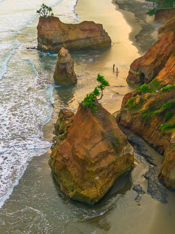 Aerial view of rock formations on a sandy beach with waves crashing against the shore and two people walking along the coastline during golden hour in Bali Bali Indonesia. Aerial view of rock formations on a sandy beach with waves crashing against the shore and two people walking along the coastline during golden hour in Bali Bali Indonesia.