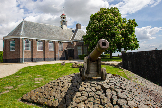 View of the historic Middelbuurt church and a vintage cannon on a stone mound under a cloudy sky in Schokland Flevoland Netherlands.