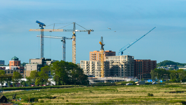 Aerial view of tower cranes at a construction site of modern residential buildings near the Oosterdel nature reserve under a clear blue sky Broek op Langedijk Noord Holland Netherlands. Aerial view of tower cranes at a construction site of modern residential buildings near the Oosterdel nature reserve under a clear blue sky Broek op Langedijk Noord Holland Netherlands.